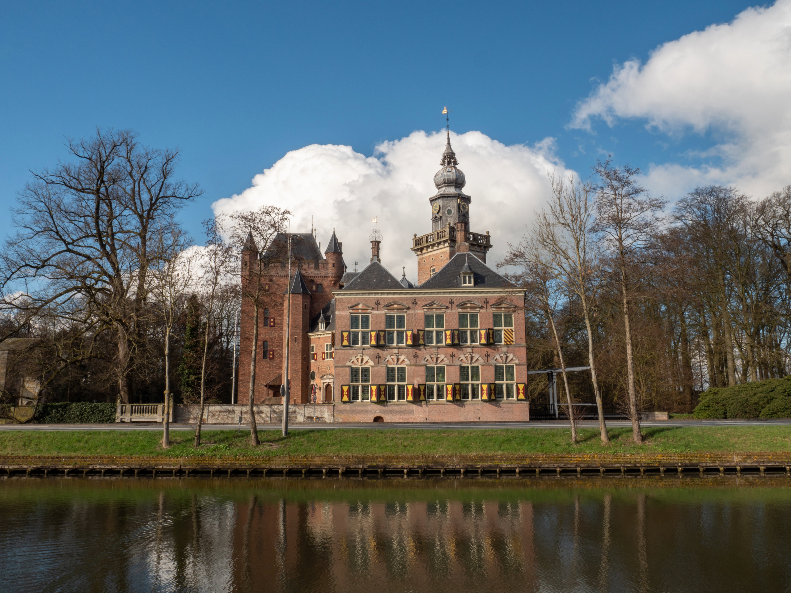 Historisch gebouw van Nyenrode aan het water, met toren, bakstenen gevel en kale bomen onder een blauwe lucht.