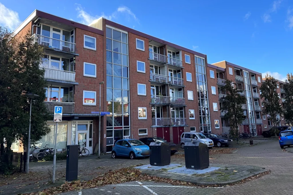 Appartementencomplex met vier woonlagen en glazen trappenhuizen, gezien vanaf het parkeerterrein
